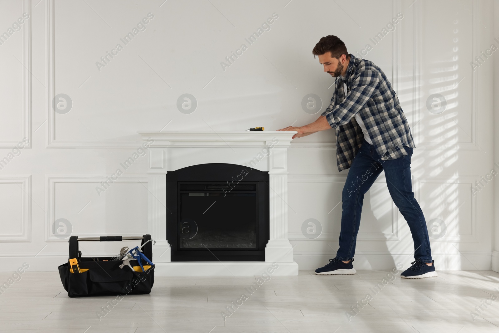 Photo of Man installing electric fireplace near white wall in room