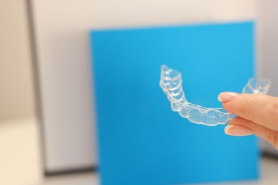 Photo of Woman with transparent dental aligner on blurred background, closeup. Space for text