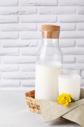 Photo of Glass and bottle of fresh milk on table against white brick wall