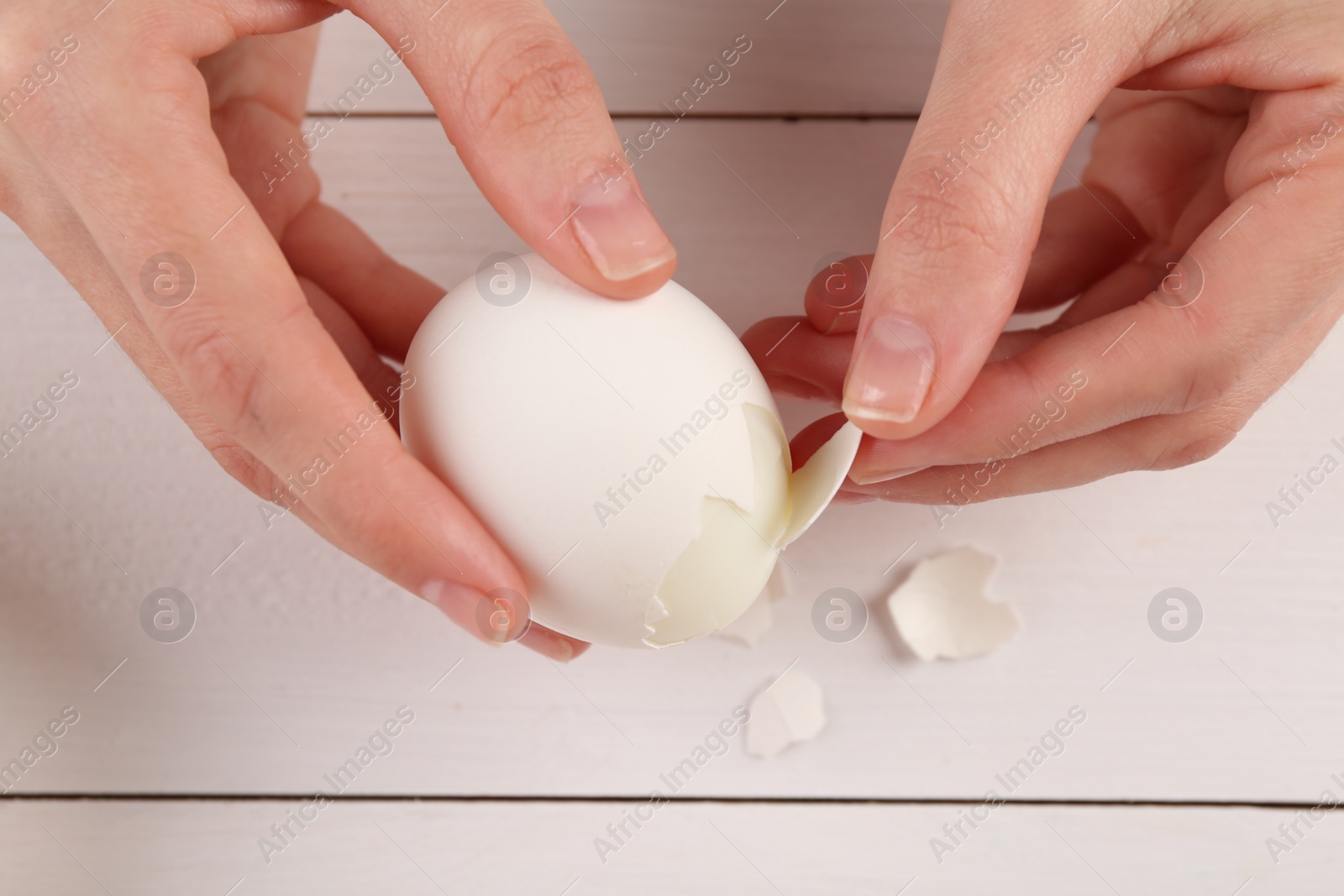 Photo of Woman peeling boiled egg at white wooden table, top view