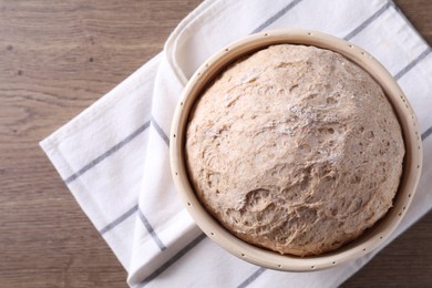 Photo of Fresh sourdough in proofing basket on wooden table, top view