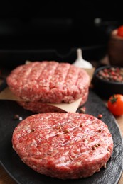 Photo of Raw hamburger patties with pepper on black board, closeup