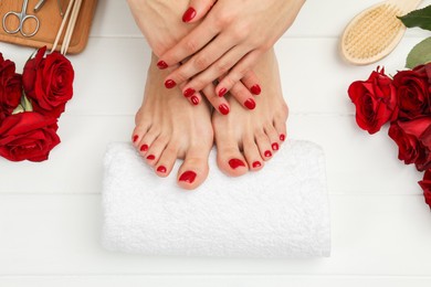 Woman with stylish red toenails after pedicure procedure and rose flowers on white wooden background, top view