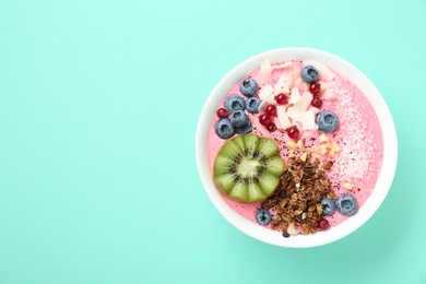 Photo of Tasty smoothie bowl with fresh kiwi fruit, berries and granola on turquoise background, top view. Space for text