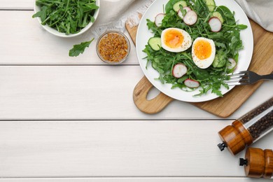 Photo of Delicious salad with boiled egg, vegetables and arugula served on white wooden table, flat lay. Space for text
