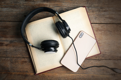 Book, modern headphones and smartphone on wooden table, flat lay