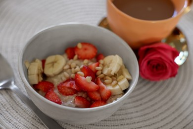 Photo of Delicious oatmeal with banana, strawberries, nuts and cup of hot drink on table, closeup
