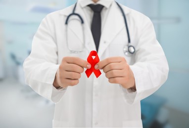 Image of Cancer awareness. Doctor holding red ribbon on blurred background, closeup