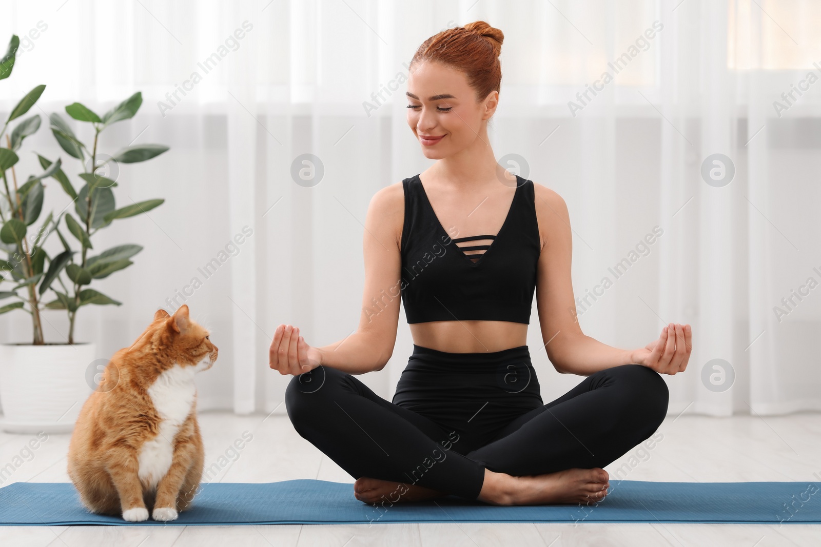 Photo of Beautiful woman with cute red cat practicing yoga on mat at home