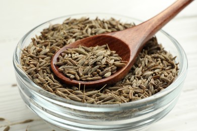 Bowl of caraway seeds and spoon on white table, closeup