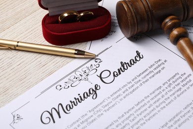 Photo of Marriage contract, golden wedding rings, pen and gavel on wooden table, closeup