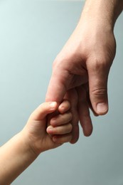 Father and child holding hands on light blue background, closeup