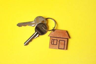 House keys with trinket on color background, top view