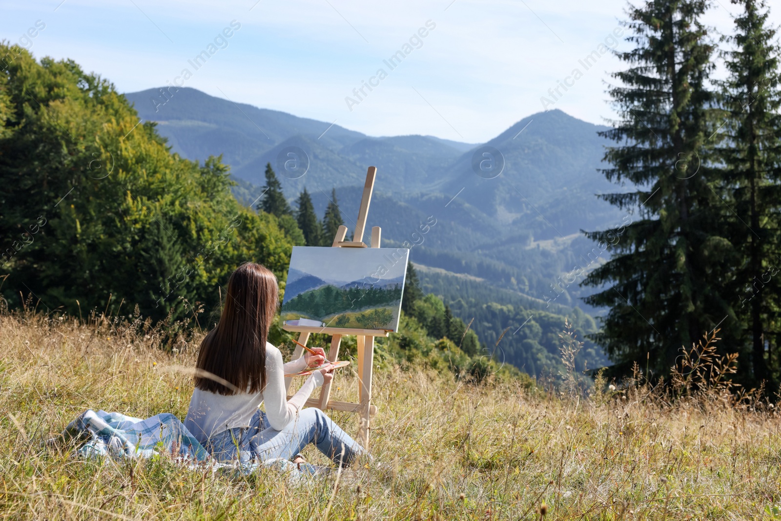 Photo of Young woman drawing on easel in mountains, back view. Space for text