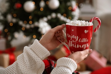 Photo of Woman with cup of delicious hot drink near Christmas tree at home, closeup