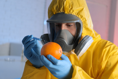 Scientist in chemical protective suit injecting orange at laboratory