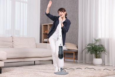 Happy young housewife having fun while cleaning carpet at home