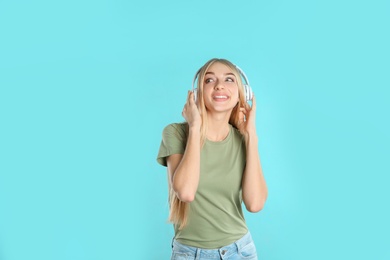 Beautiful young woman listening to music with headphones on color background