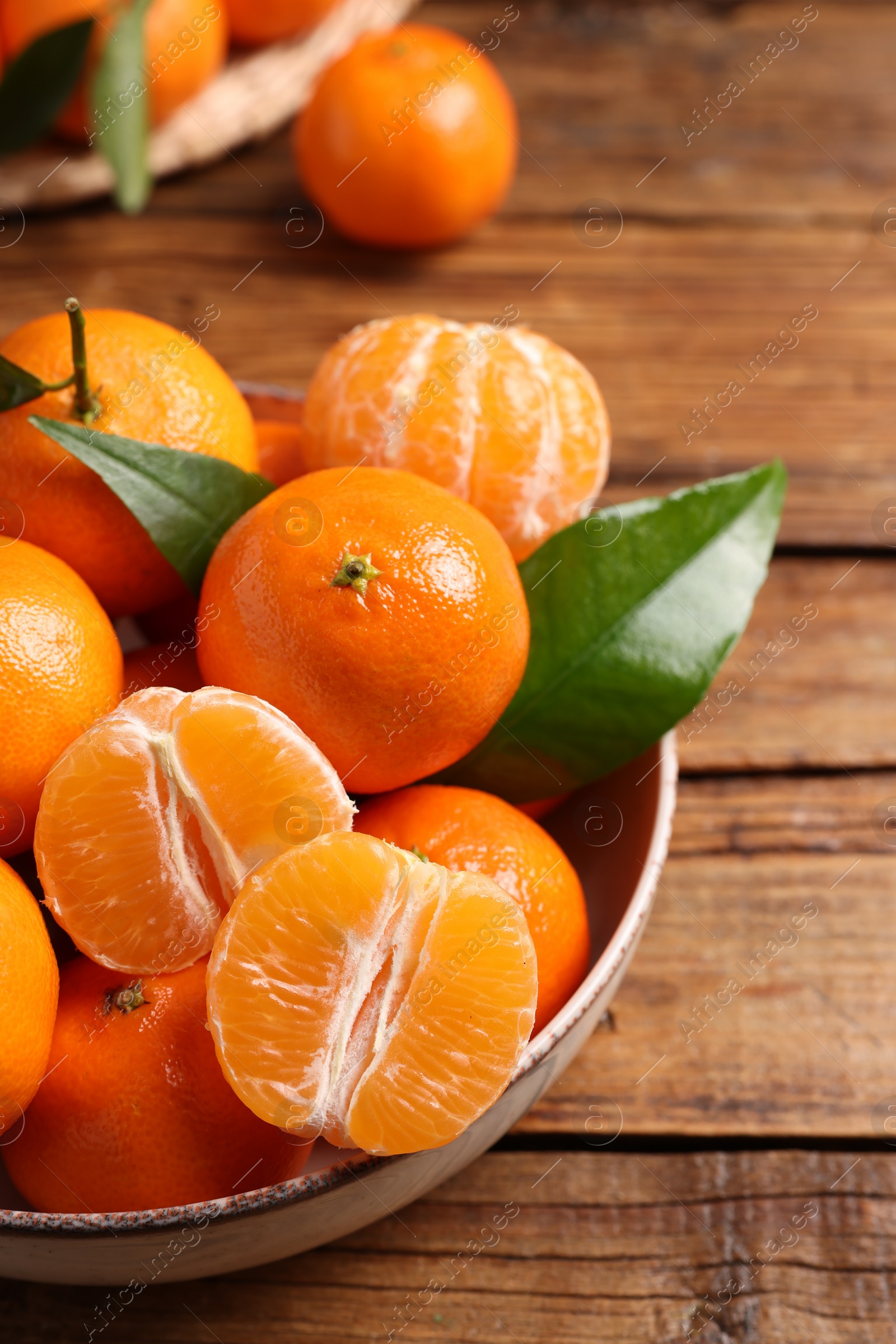 Photo of Fresh tangerines with green leaves in bowl on wooden table, closeup