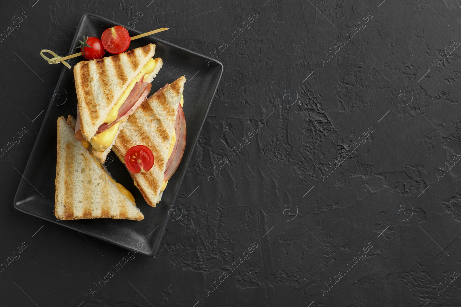 Photo of Tasty sandwiches with ham, melted cheese and tomatoes on black textured table, top view. Space for text