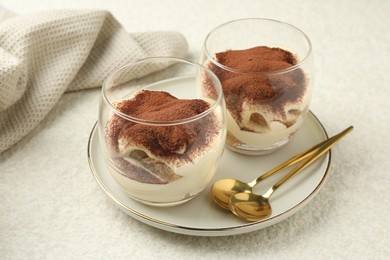 Delicious tiramisu in glasses and spoons on white table