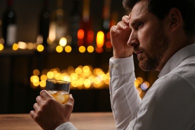 Man with glass of whiskey against blurred lights, closeup