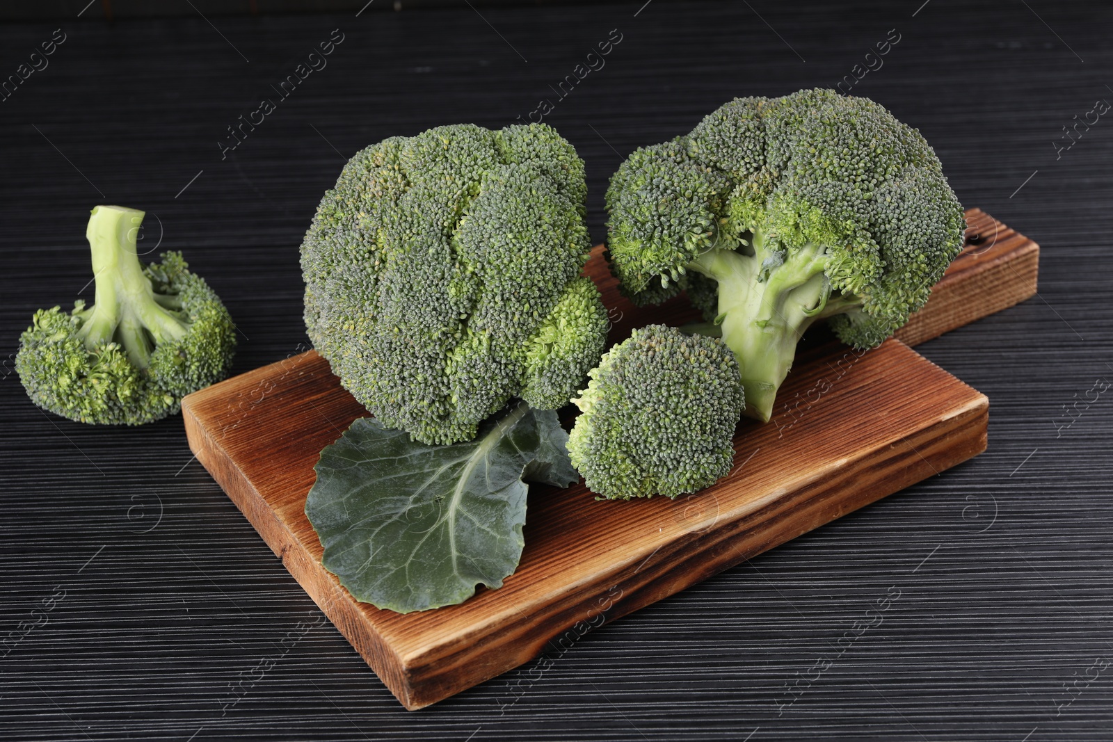 Photo of Board with fresh raw broccoli on black wooden table