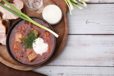 Tasty borscht with sour cream in bowl served on white wooden table, flat lay. Space for text
