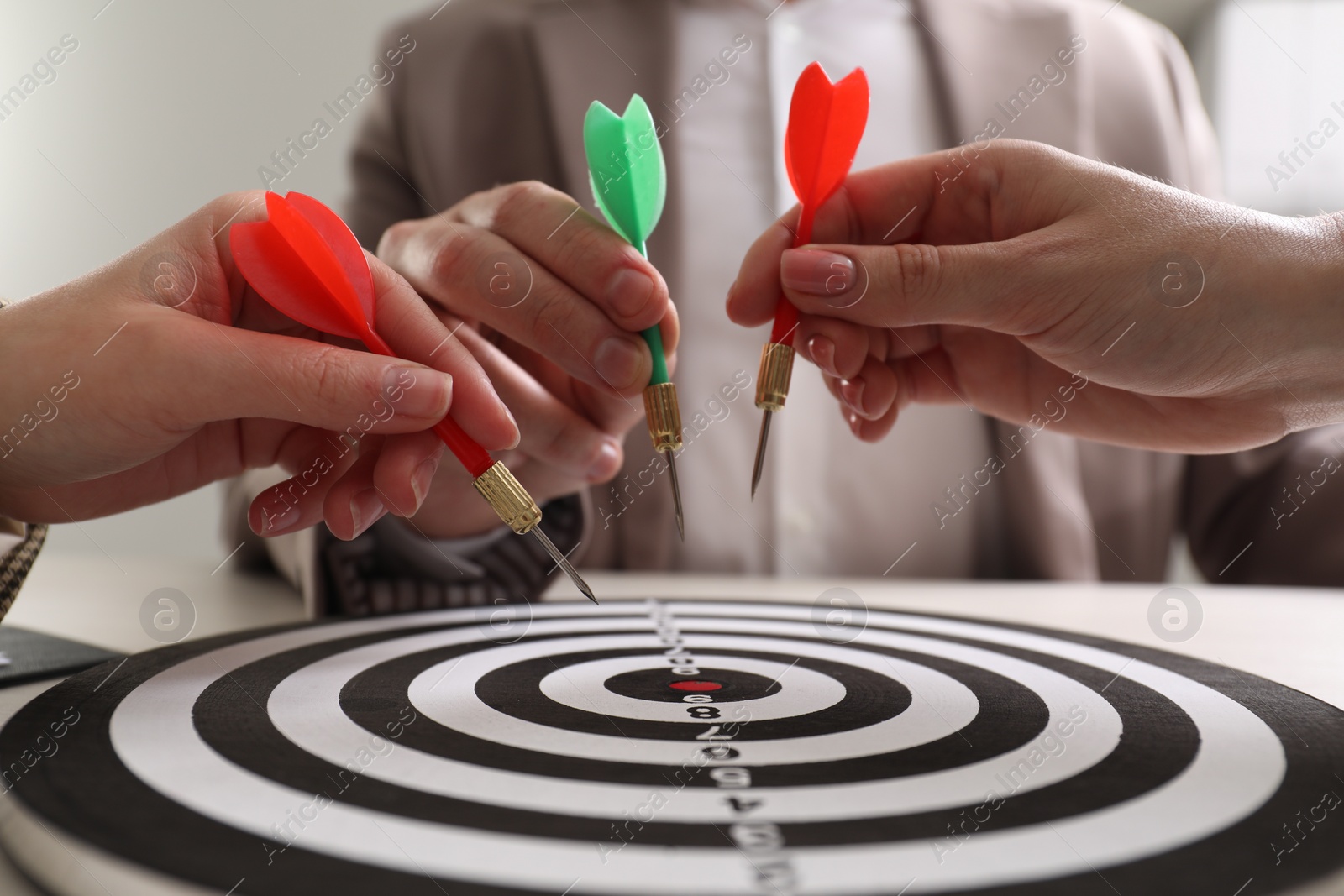 Photo of Business targeting concept. People with darts aiming at dartboard at table, closeup