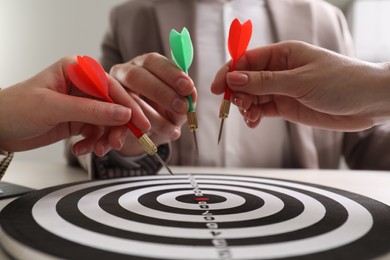 Business targeting concept. People with darts aiming at dartboard at table, closeup