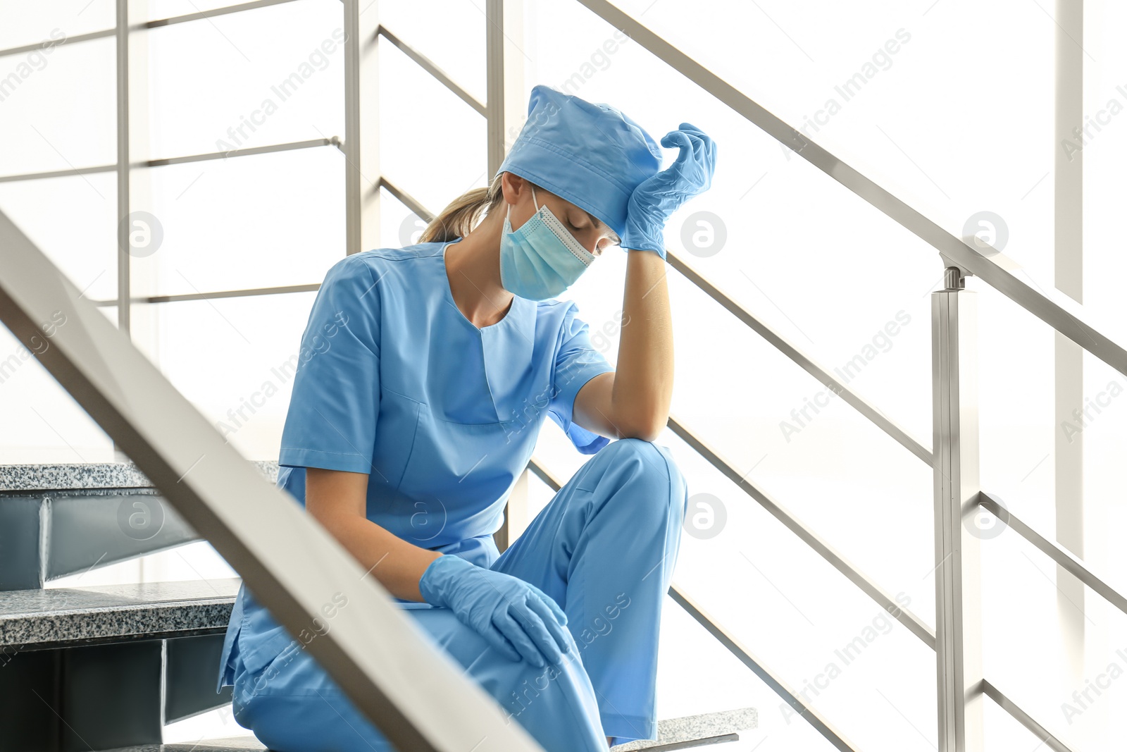 Photo of Exhausted doctor sitting on stairs in hospital. Stress of health care workers during COVID-19 pandemic