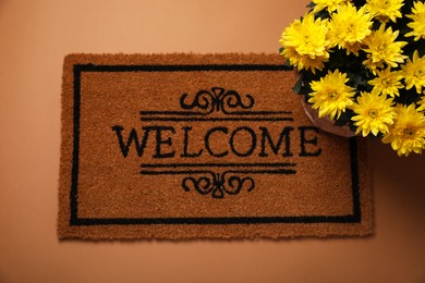 Doormat with word Welcome and flowers on brown background, flat lay
