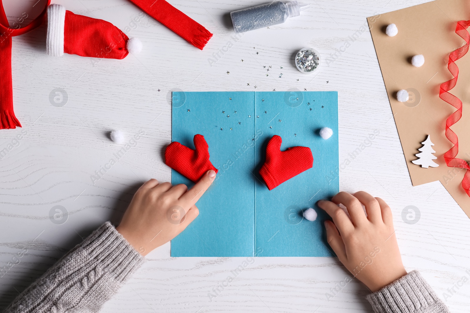 Photo of Little child making Christmas card at white wooden table, top view