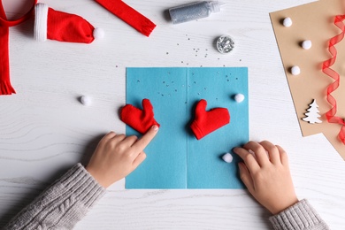 Little child making Christmas card at white wooden table, top view