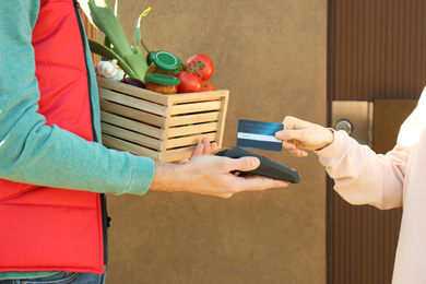 Photo of Client paying courier for fresh products with credit card outdoors, closeup. Food delivery service