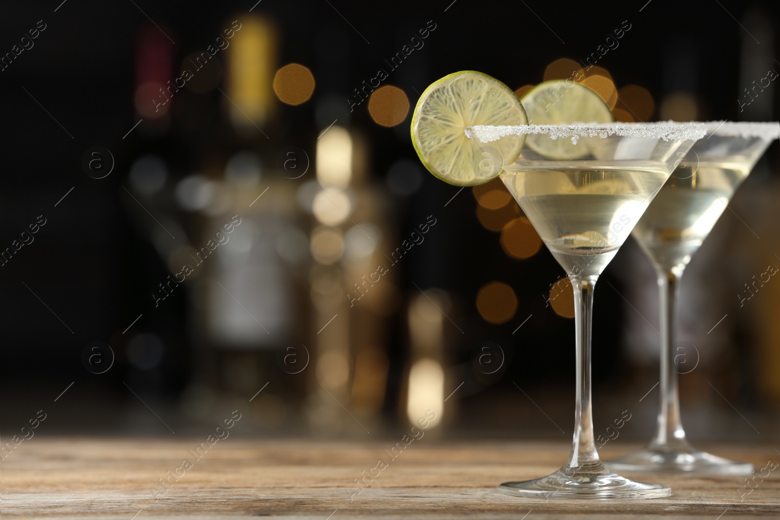 Photo of Glasses of Lime Drop Martini cocktail on wooden table against blurred background. Space for text