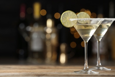 Photo of Glasses of Lime Drop Martini cocktail on wooden table against blurred background. Space for text