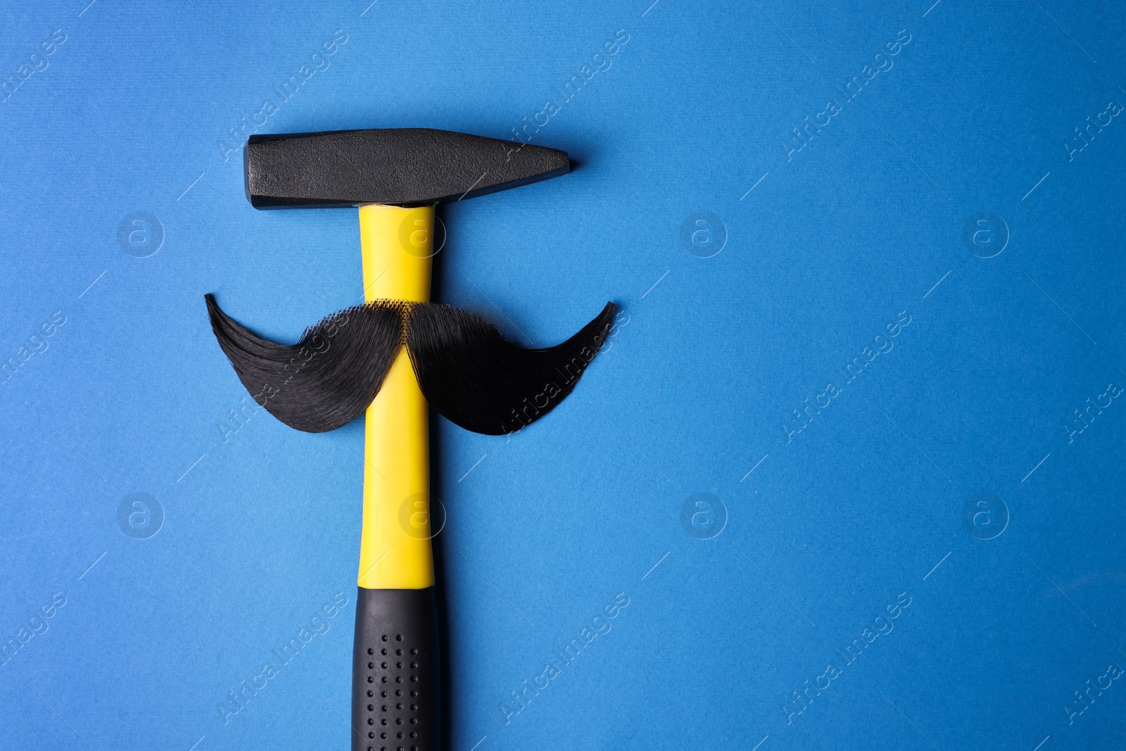 Photo of Man's face made of artificial mustache and hammer on blue background, top view. Space for text