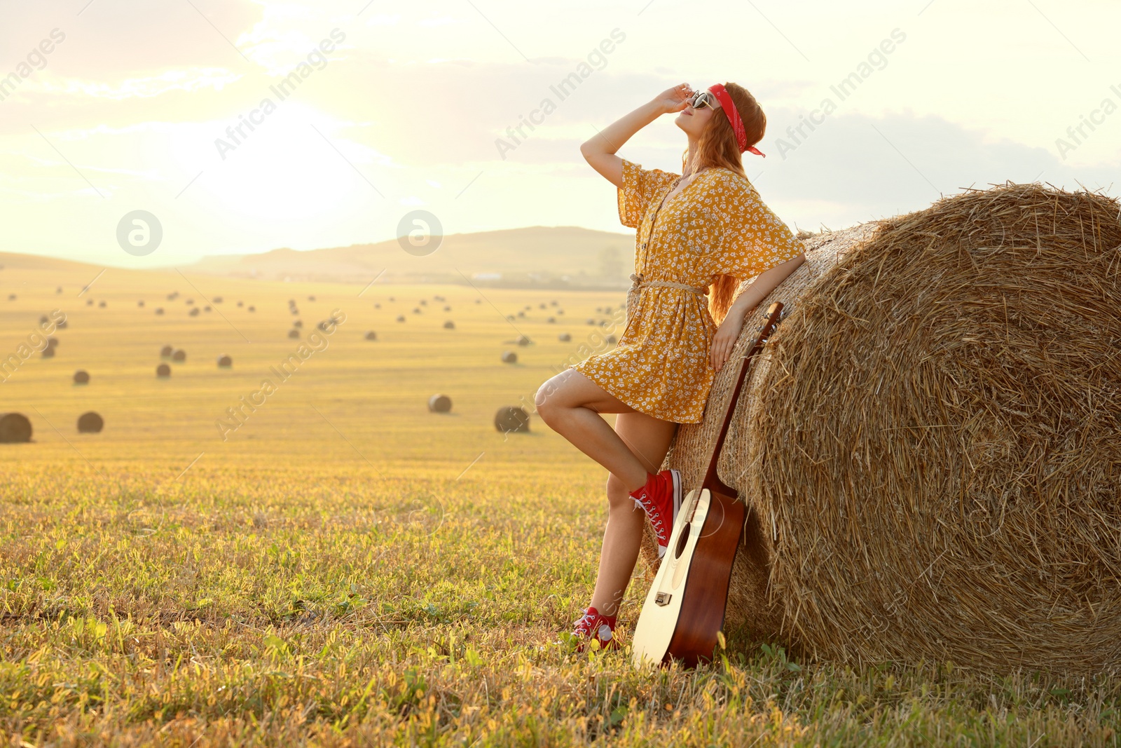 Photo of Happy hippie woman with guitar near hay bale in field, space for text