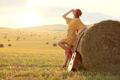 Happy hippie woman with guitar near hay bale in field, space for text