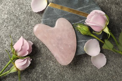 Photo of Rose quartz gua sha tool and flowers on grey table, flat lay