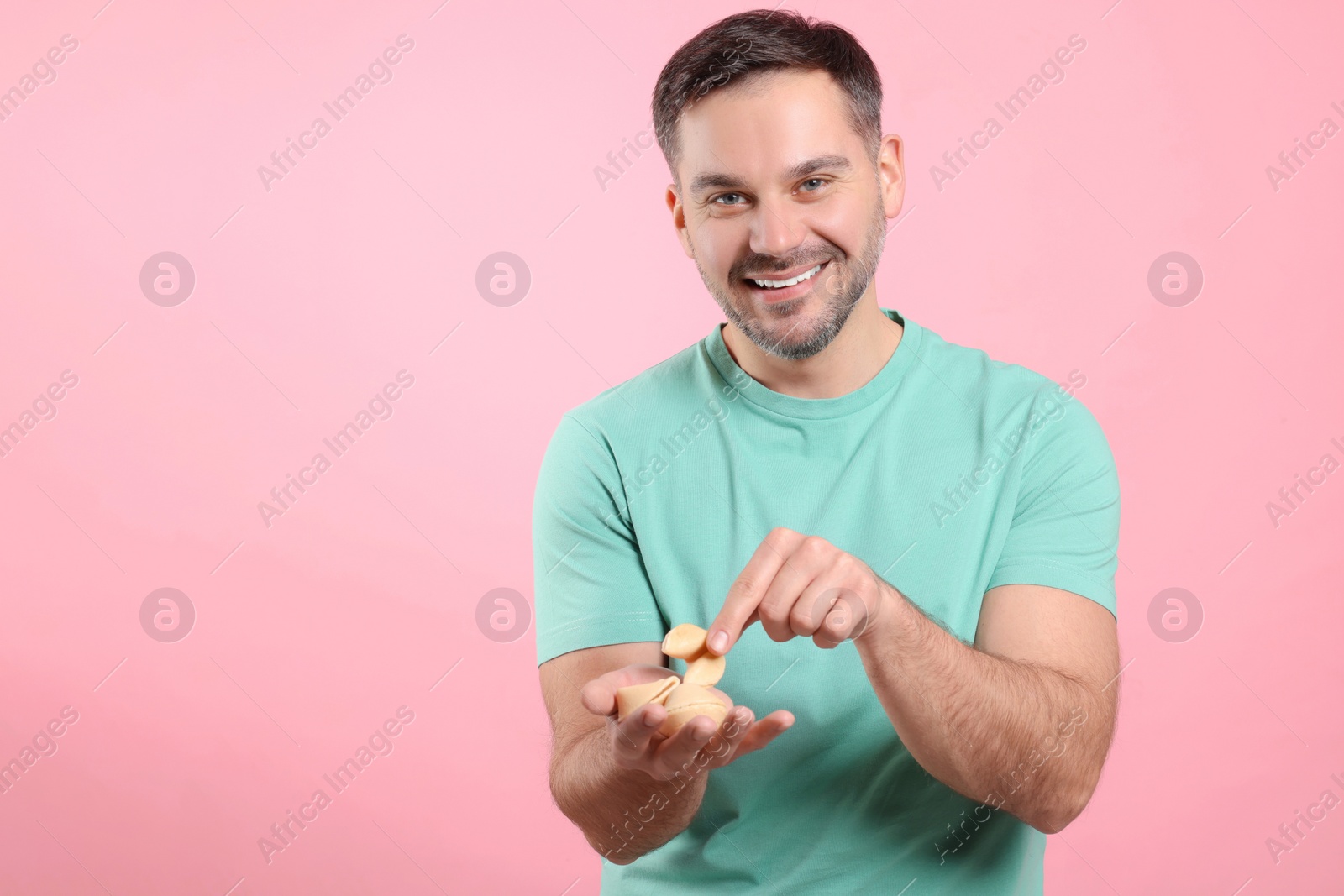 Photo of Happy man holding tasty fortune cookies with predictions on pink background. Space for text