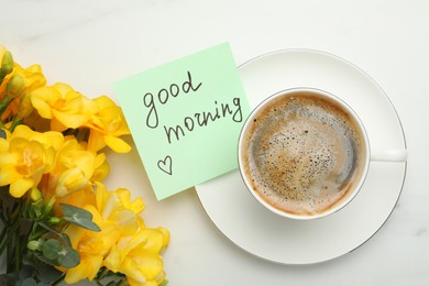 Photo of Cup of aromatic coffee, beautiful yellow freesias and Good Morning note on white marble table, flat lay