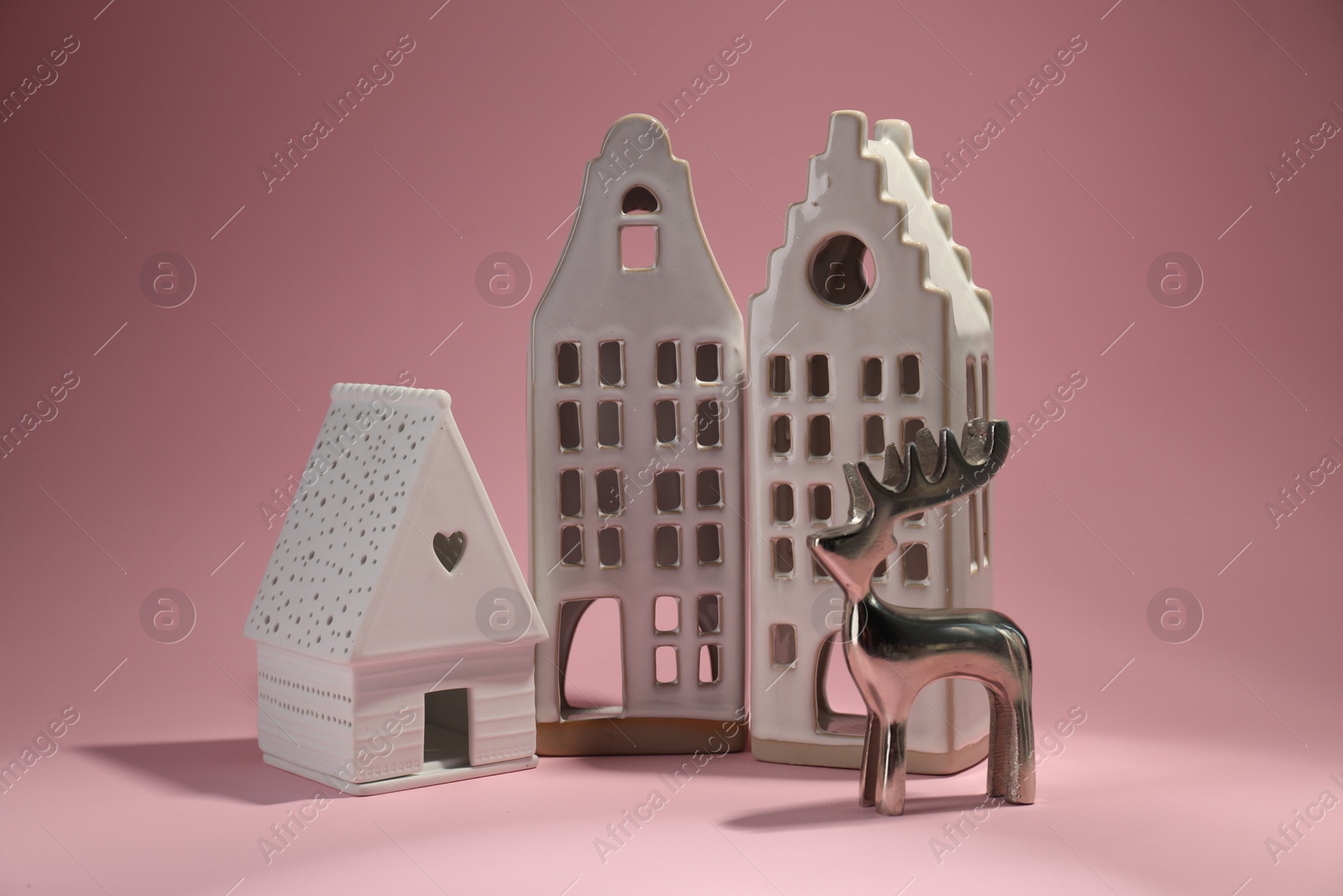 Photo of House shaped candle holders and silver deer on pink background