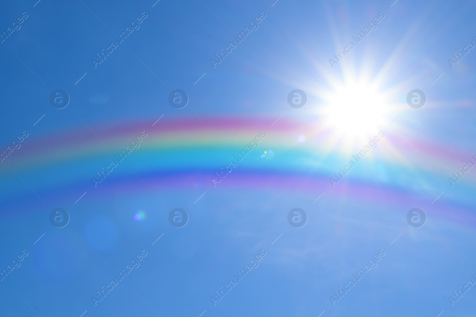 Image of Beautiful view of bright rainbow in blue sky on sunny day