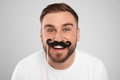 Funny man with fake mustache on light grey background