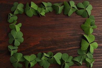 Photo of Frame of clover leaves on wooden table, top view with space for text. St. Patrick's Day symbol