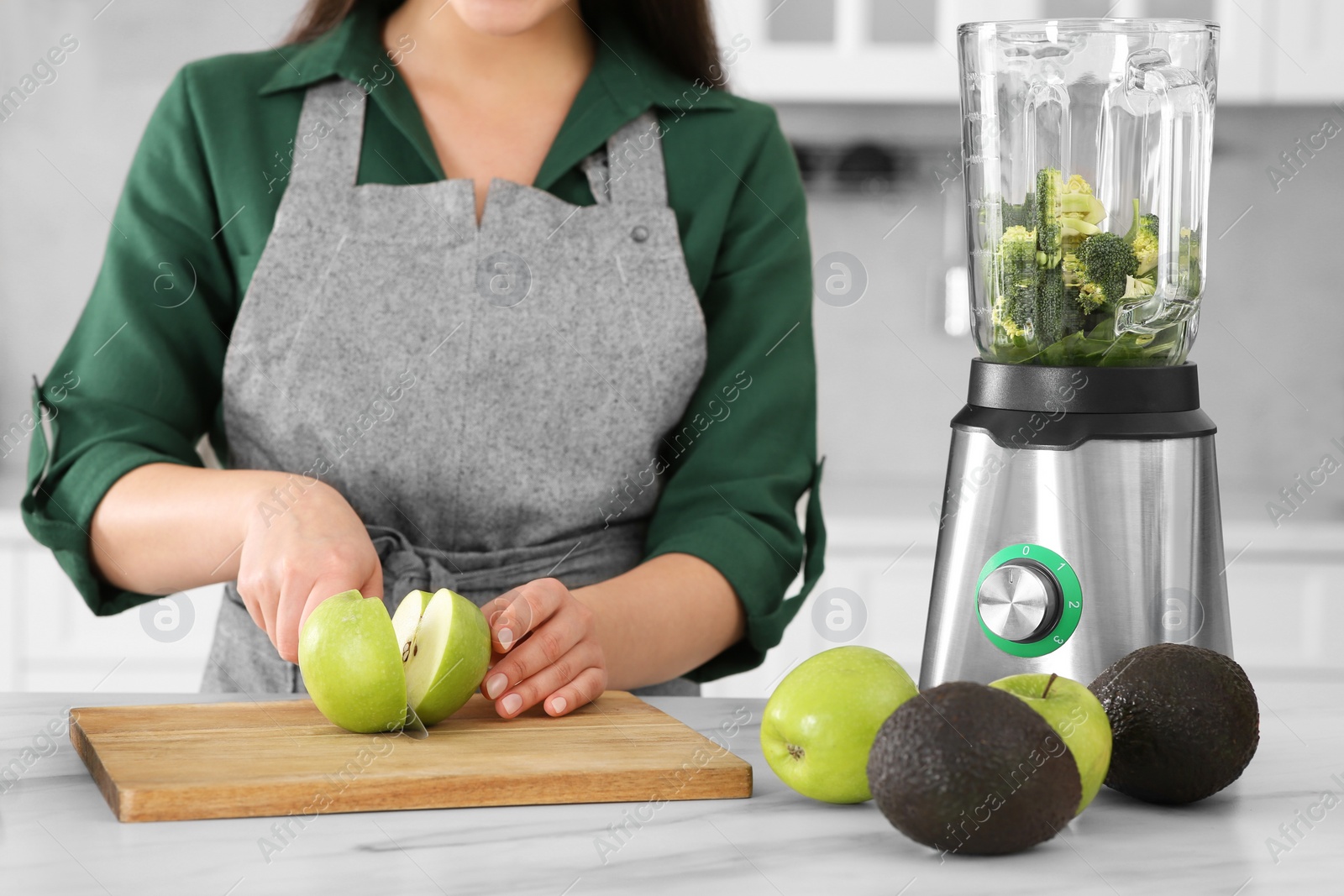 Photo of Young woman cutting apple for smoothie at white table in kitchen, closeup