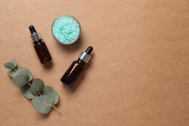 Photo of Aromatherapy products. Bottles of essential oil, sea salt and eucalyptus branch on brown background, flat lay. Space for text