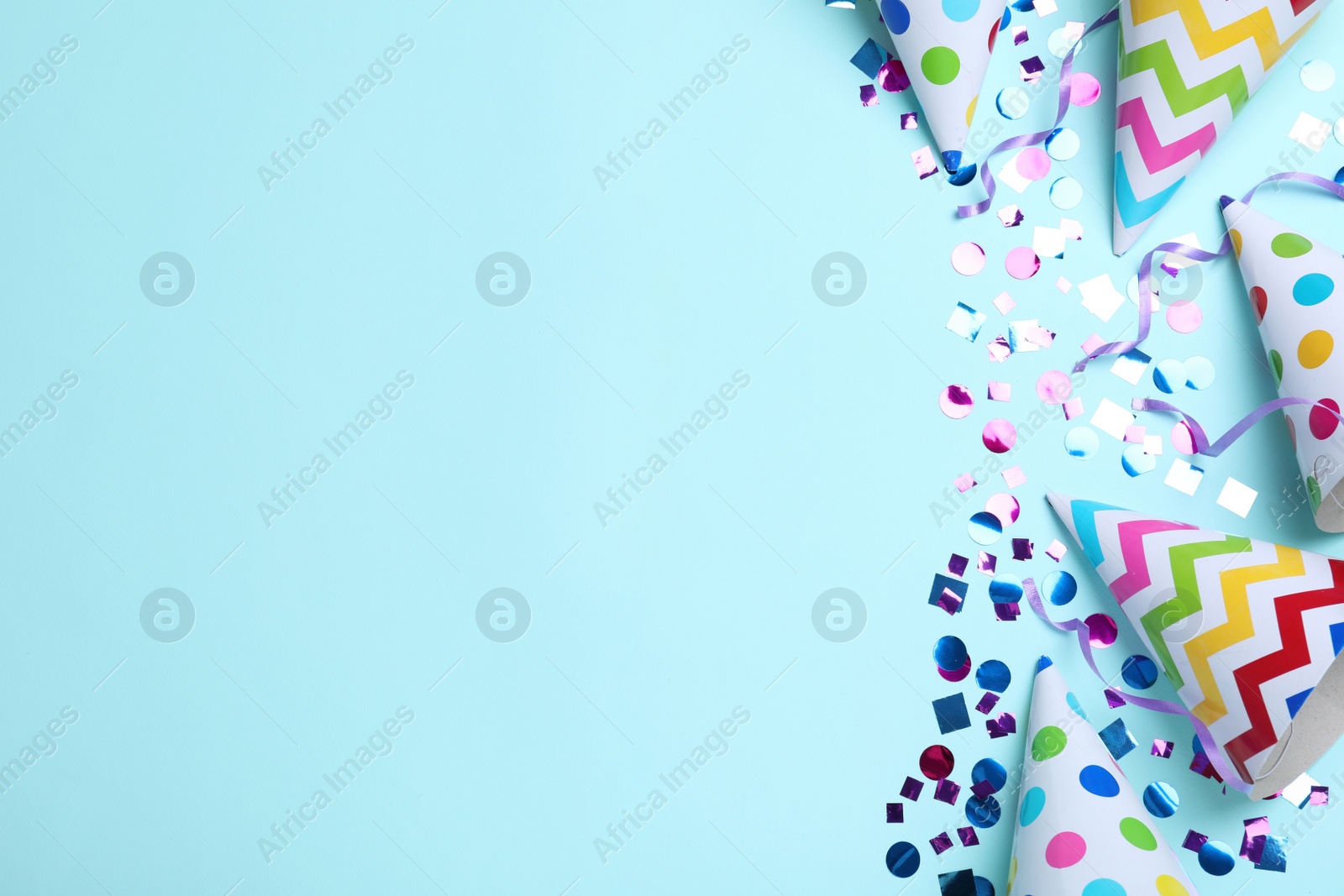 Photo of Flat lay composition with party hats and confetti on light blue background, space for text. Birthday items